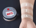 Emelie Matte Loose Powder container with swatches on a wrist against a dark background