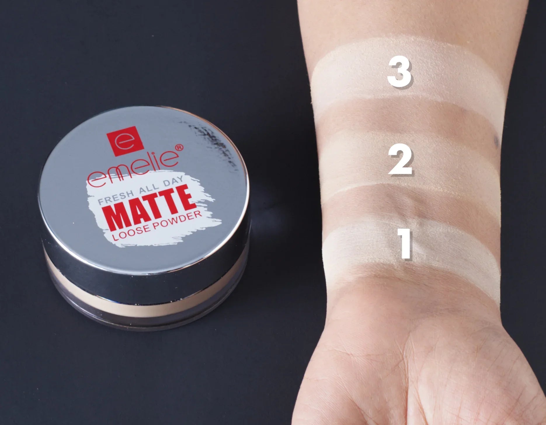 Emelie Matte Loose Powder container with swatches on a wrist against a dark background