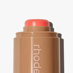 Cosmetic stick with coral-colored cap on a white background, featuring the brand 'rhode'.